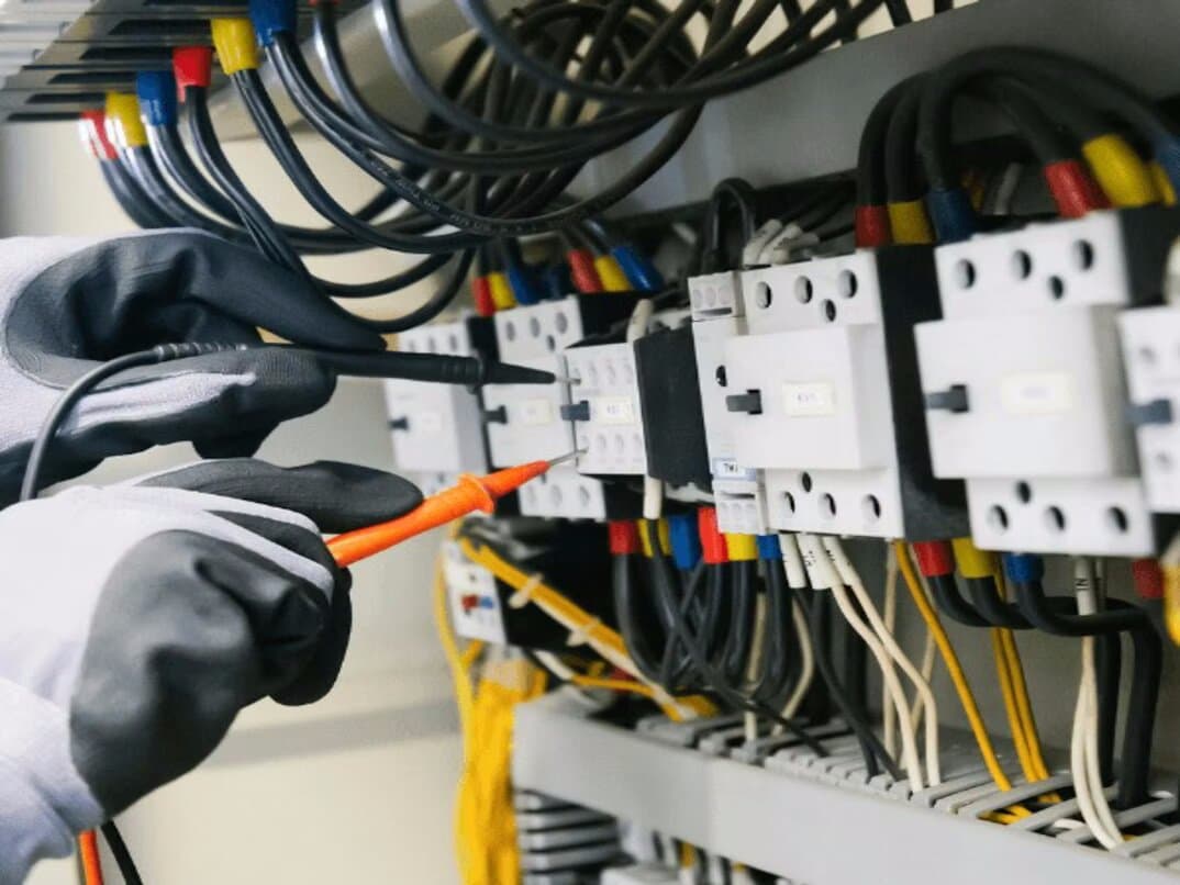 Electrician working inside a control panel with circuit breakers, contactors, and wiring — where a QRchive sticker provides instant access to documentation
